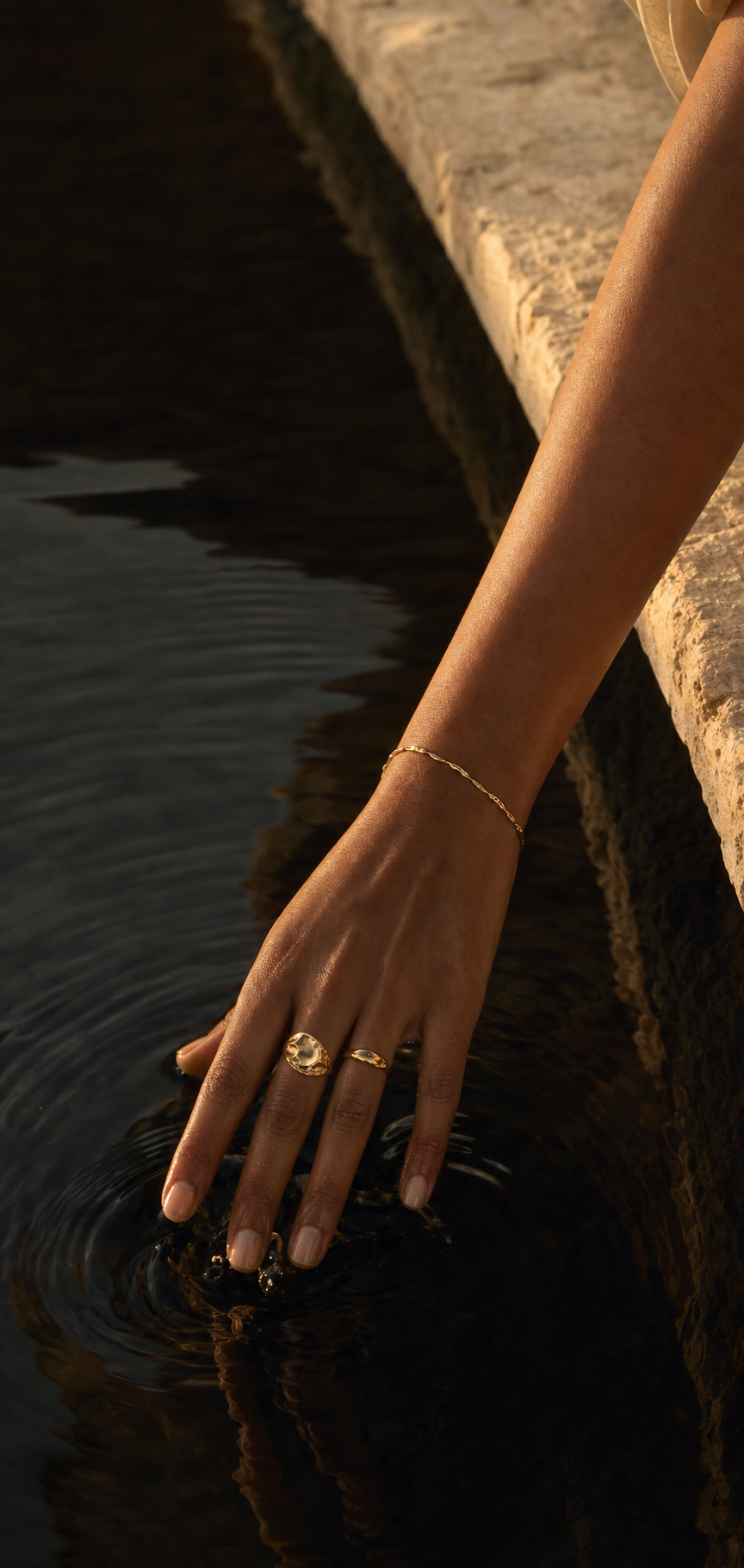A hand wearing gold jewelry touching water